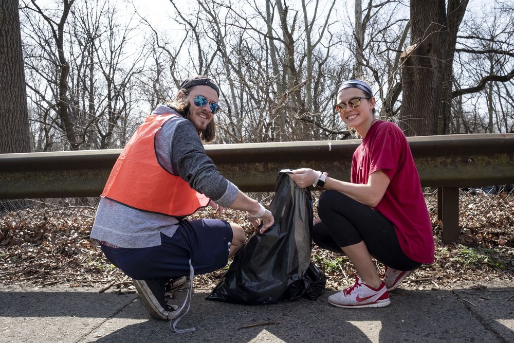 Two students participate in a cleanup. Both are holding a bag of litter, smiling at the camera.