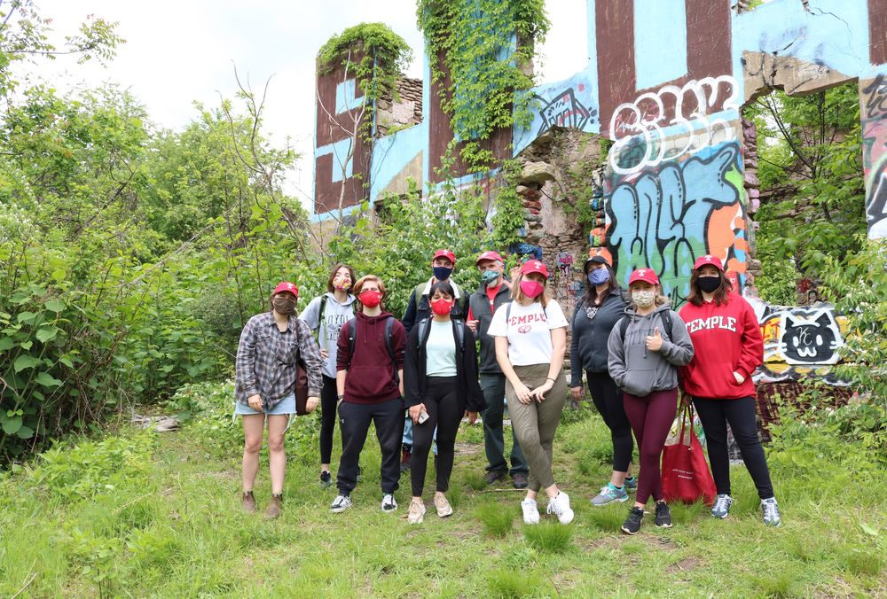 group of Temple students poses in front of graffitied mansion on Sedgley woods disc golf course